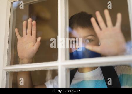 Caucasian boy looking through window and wearing face mask Stock Photo