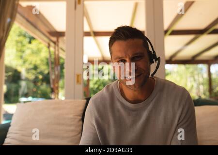 Portrait of caucasian man working from home wearing a phone headset sitting in living room and smili Stock Photo