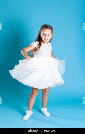 full-length portrait of girl in a white angel dress with swirling skirt and dancing, with Christmas makeup on her face, isolated on a blue background Stock Photo