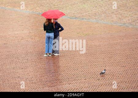 Two women huddled under a red umbrella on a rainy day in the Piazza del Campo, Siena, Tuscany, Italy Stock Photo