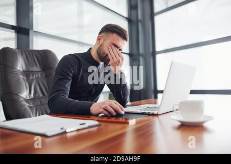 Man in formal clothes sitting by the table with laptop and feels bad Stock Photo
