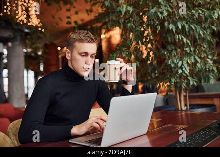 Successful young guy sits in cafe by table with his laptop on it Stock Photo