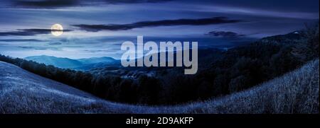 mountainous countryside at night. beautiful panorama of carpathians. valley of borzhava ridge in the distance in full moon light. clouds on the sky Stock Photo