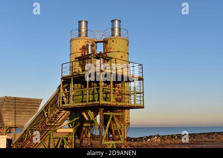 Old dismantled equipment where they molded concrete. It stands on the beach near Rome. Rusty wreck of metal in a shiny morning with very neat horizon Stock Photo