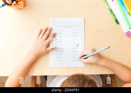 Top view of child hands with pencils. Solving maths exercises. 7 years old child doing maths lessons sitting at desk in his room. Stock Photo