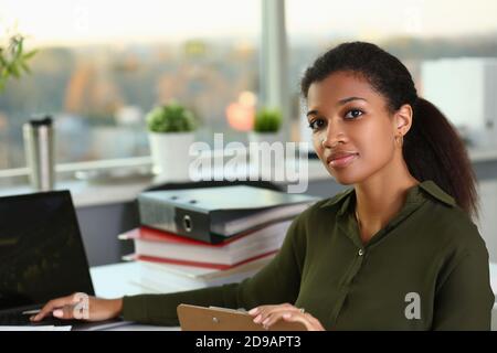 African woman businesswoman sits behind steel worker holds clipboard pen near laptop Stock Photo
