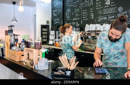 Waitress preparing coffee machine while her coworker uses the tablet Stock Photo