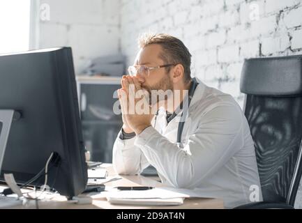 The doctor sits in the office in front of the monitor. He looks thoughtfully and sadly at the monitor. Bad news. Stock Photo
