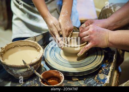 the Hands of a master and a student make a pitcher on a Potters wheel of yellow clay. Selective focus on hands Stock Photo