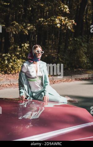 Elegant woman in sunglasses sitting on bumper of vintage car outdoors Stock Photo