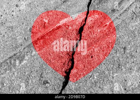 Red heart on a cracked texture. The concept of broken heart, end of love and disappointment. Stock Photo