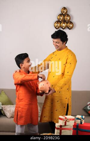 handsome Indian/asian father teaching importance of saving to his kid at home with piggy bank. Stock Photo