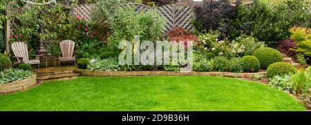 Landscaped private garden (contemporary design, summer flowers, border plants & shrubs, patio furniture, curving lawn, fence) - Yorkshire, England, UK Stock Photo