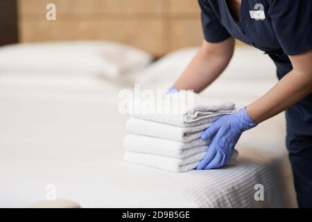 Cropped photo of maid in uniform putting towels on the bed in hotel apartment. Hotel service concept Stock Photo