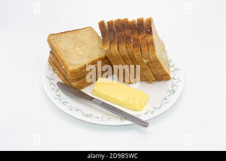 Slices of freshly baked bread and salted butter with butter knife kept on a plate with white background Stock Photo