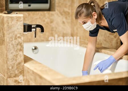 Maid in protective gloves cleaning bathroom in a hotel room. Hotel service concept Stock Photo