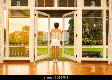 Women opening glass door to refreshing sunrise with greenaries Stock Photo