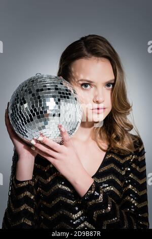 young woman looking at camera while holding disco ball on grey Stock Photo