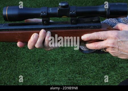 Close up mature woman's hands holding a rifle on a grass background with copy space at the bottom of the image Stock Photo