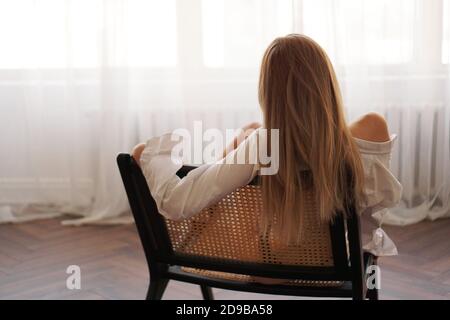 Beautiful young woman relaxing, leaning back in chair at home, looking at window Stock Photo