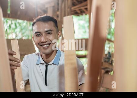 close up of a carpenter working smiling between the legs of a wooden chair at the workshop Stock Photo