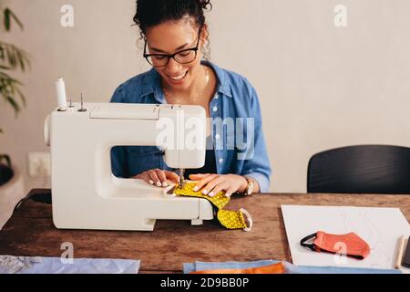 Woman working at home sewing face masks. Female tailor preparing protective face masks on a sewing machine at home. Stock Photo