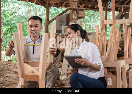 carpenter measuring wood using ribbon ruler with owner woman using tablet pc at the workshop Stock Photo