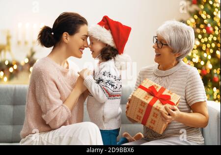 Premium Photo  Merry christmas and happy holidays! cheerful grandma and  her cute grand daughter girl exchanging gifts. granny and little child  having fun near tree indoors. loving family with presents in