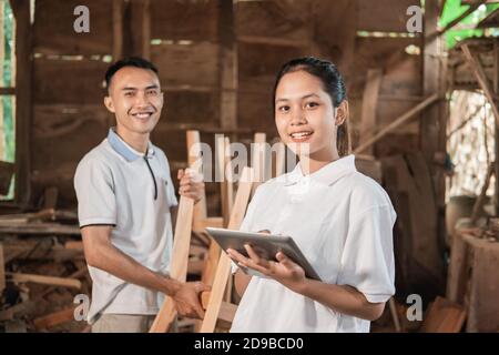smiling women entrepreneurs standing holding a tablet pc and workers standing behind while in the workshop Stock Photo