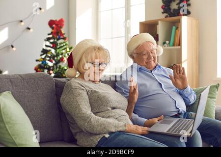 Happy senior couple sitting on couch at home, video calling family and waving hands Stock Photo