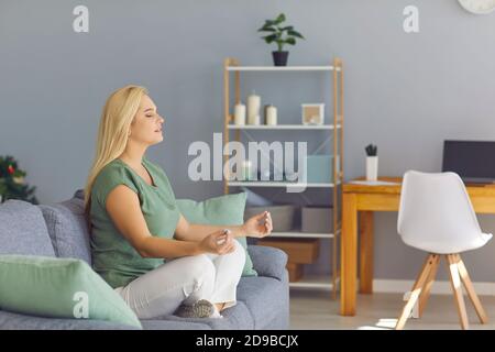 Happy young woman relaxing on couch, meditating in cross-legged pose, enjoying inner peace Stock Photo