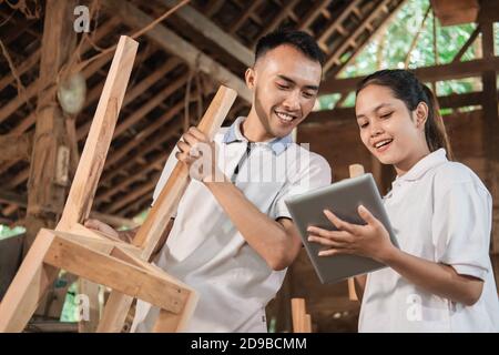 young entrepreneur holding a tablet and showing furniture designs to a carpenter at the workshop Stock Photo