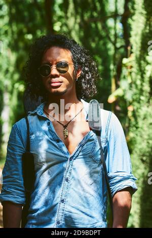 Musician walking with the guitar hanging on his back. He is walking in a park with vegetation. Stock Photo