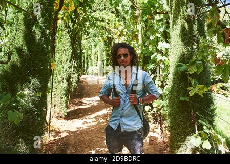 Musician walking with the guitar hanging on his back. He is walking in a park with vegetation. Stock Photo