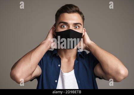 Photo of scared young man isolated over grey wall background in a mask Stock Photo