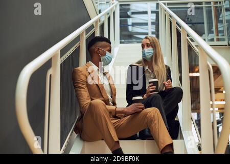 Business Couple Wearing Masks Meet On Office Stairs During Break In Office During Pandemic Stock Photo