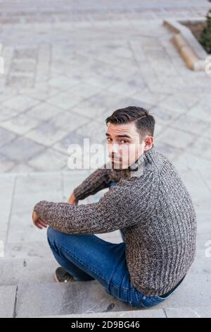 White man in autumn vest sitting on a single-place fountain Stock Photo