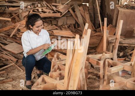 young asian woman smiles while using her tablet pc in a furniture workshop Stock Photo