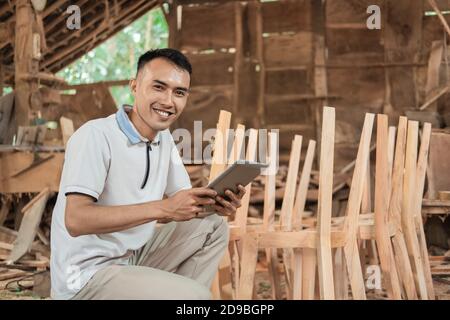 Furniture entrepreneur smiles looking at the camera while using a tablet pc in a furniture workshop Stock Photo
