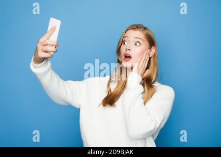 shocked blonde beautiful woman taking selfie isolated on blue background Stock Photo
