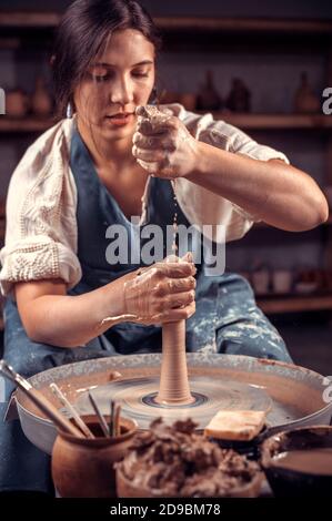 Charming young woman master shows how to work with clay and pottery wheel. Concept for woman in freelance, business, hobby. Stock Photo