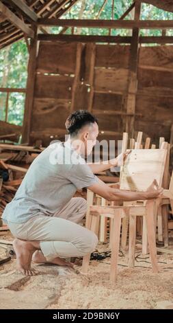 carpenter squats when assembling some wood made chairs in the workshop Stock Photo