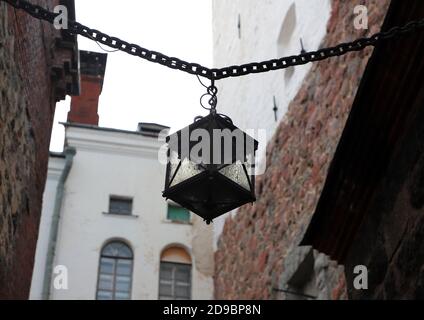 An old black lamp, hanging on chains in a medieval castle. White wall with windows in the background. Stock Photo
