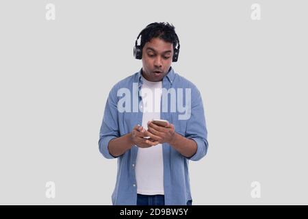Indian Man Listening Music and Chatting on Phone Surprised. Man is Suprised by Music from Phone. Man with Phone in Hands Isolated. Music Concept Stock Photo