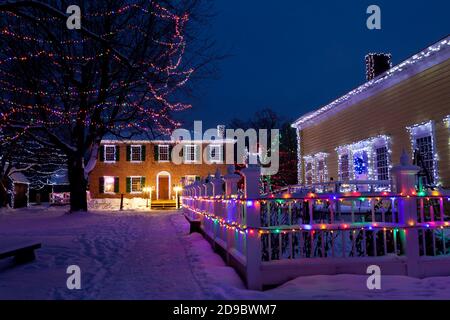 Heritage buildings, trees and fences decorated with Christmas lights at Upper Canada Village, Morrisburg, Ontario, Canada Stock Photo