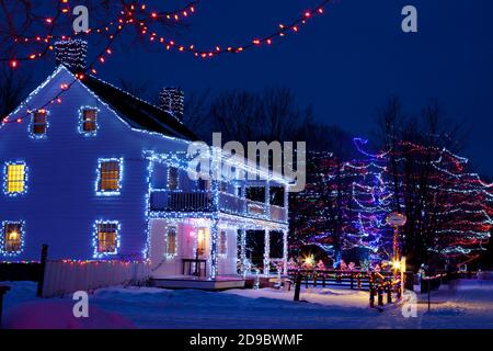 Heritage buildings, trees and fences decorated with Christmas lights at Upper Canada Village, Morrisburg, Ontario, Canada Stock Photo