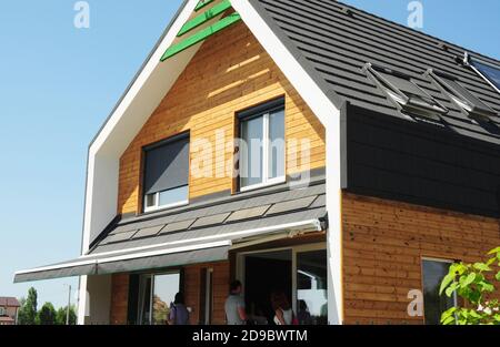 Modern energy efficient wooden house with skylights and solar panel on asphalt shingled roof, windows with roller shutters and outdoor canopy roof. Stock Photo