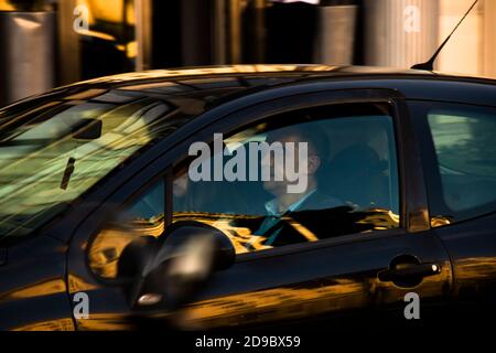 Belgrade, Serbia - October 9,  2020: Mature couple driving in a black car on city street, through window with reflections and blurs of a golden day Stock Photo