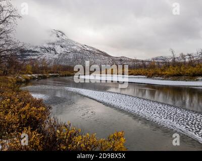 Sand bank with snow in a shallow Rapa river with snow covered mountains and autumn colors, Sarek National park, Sweden Stock Photo