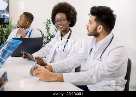 Cropped image of team of multiethnic doctors, looking doctor speech at digital screen on video conference at light room. Focus on pretty smiling Stock Photo